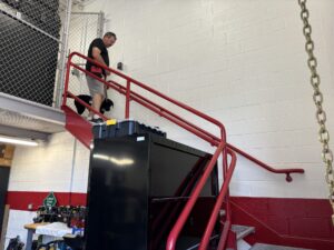 A man and his black Labrador puppy walk down red emergency stairs.