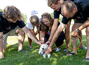 The Fisher family leans down to pet a yellow lab puppy, Forrest, on grass