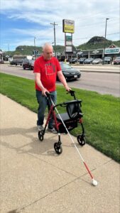 David using his rollator walker and white cane on a sidewalk