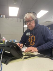 A person wearing a headset writing on a notepad at their desk, in an office environment.