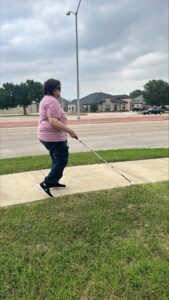 Judy walking on a sidewalk with her white cane.