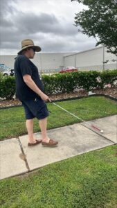 Kevin with his white cane walking along a sidewalk