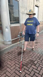 Kevin with his white cane walking on a brick sidewalk