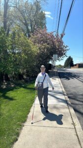 Sandy walking down a sidewalk with her white cane
