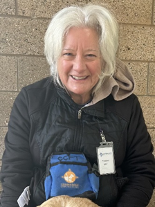 A person with short white hair wearing a winter coat and a Leader Dog badge smiles at the camera.