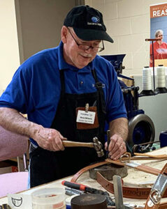 Steve Williams works in the tack shop with a hammer and other tools to assemble a leather harness