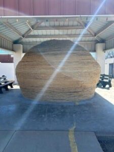 Large twine ball on display under a shelter with benches around it.