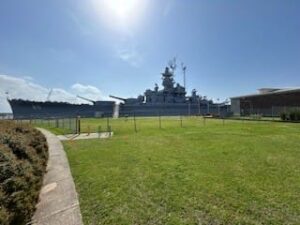 The Battleship USS Alabama, moored in Mobile Bay under bright sunshine and a cloudless, blue sky.