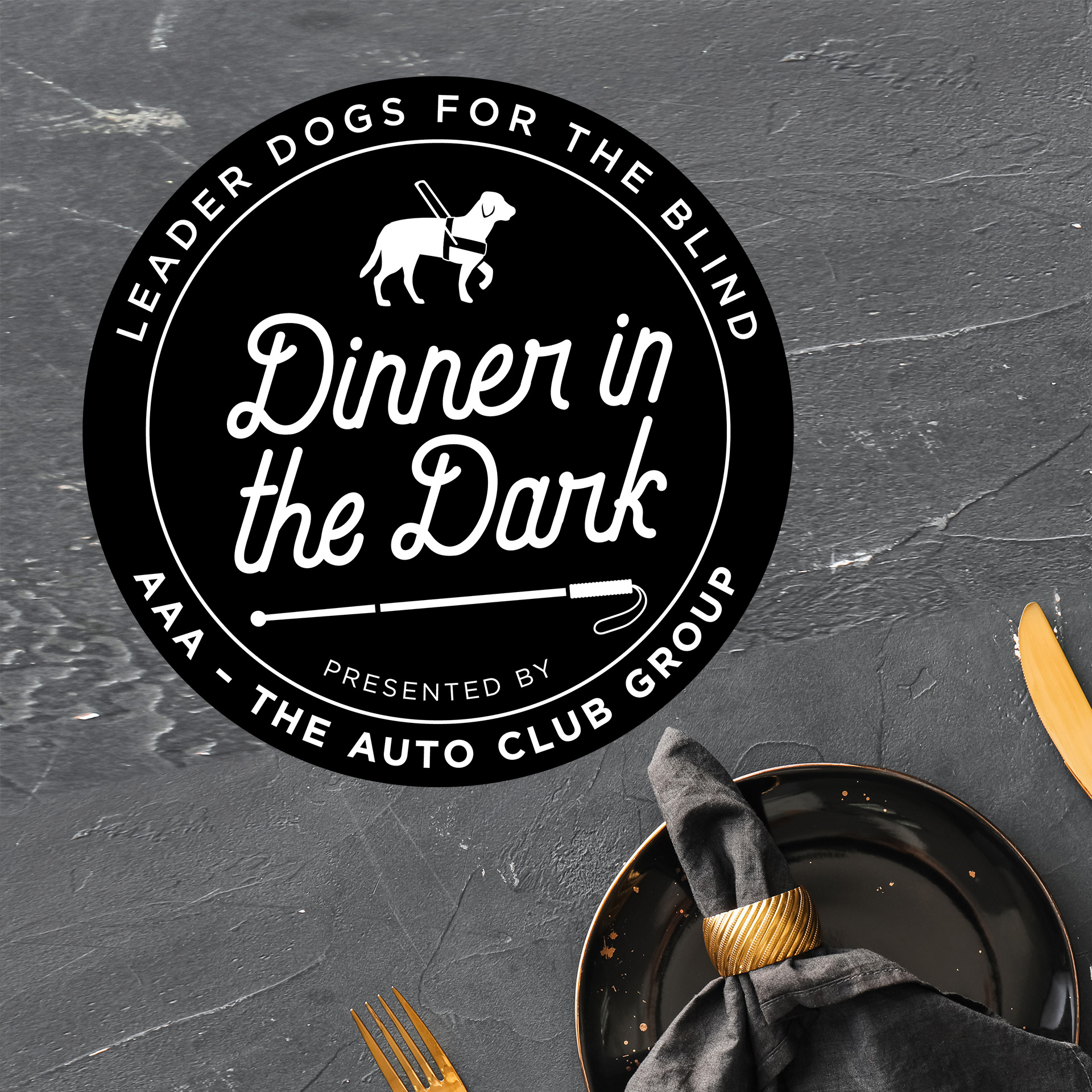Dinner in the Dark graphic featuring the event logo and a slate background with a gold place setting peeking through the bottom corner. The logo is in black and white and features a silhouette of a guide dog and white cane.