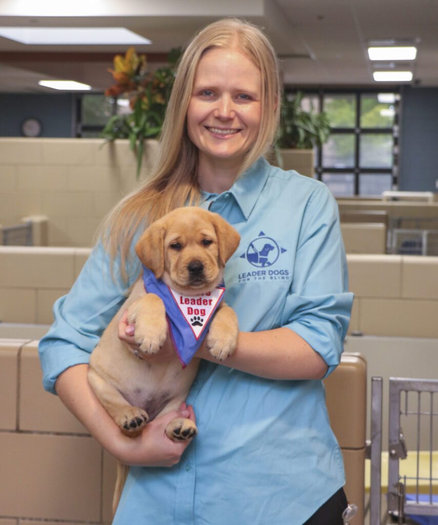 A person holding a cute puppy wearing a bandana, both smiling in a bright indoor setting.