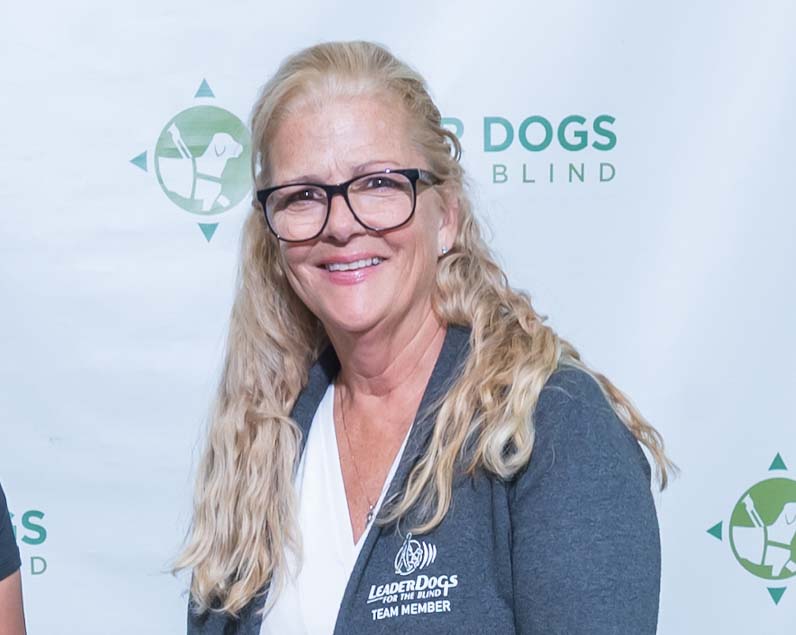 A woman with long, blond, curly hair smiles toward the camera.