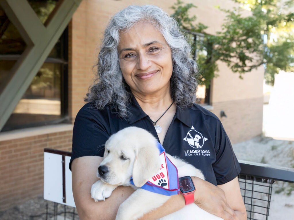 A person with curly gray hair smiles while holding a fluffy yellow puppy, both radiating warmth and joy.