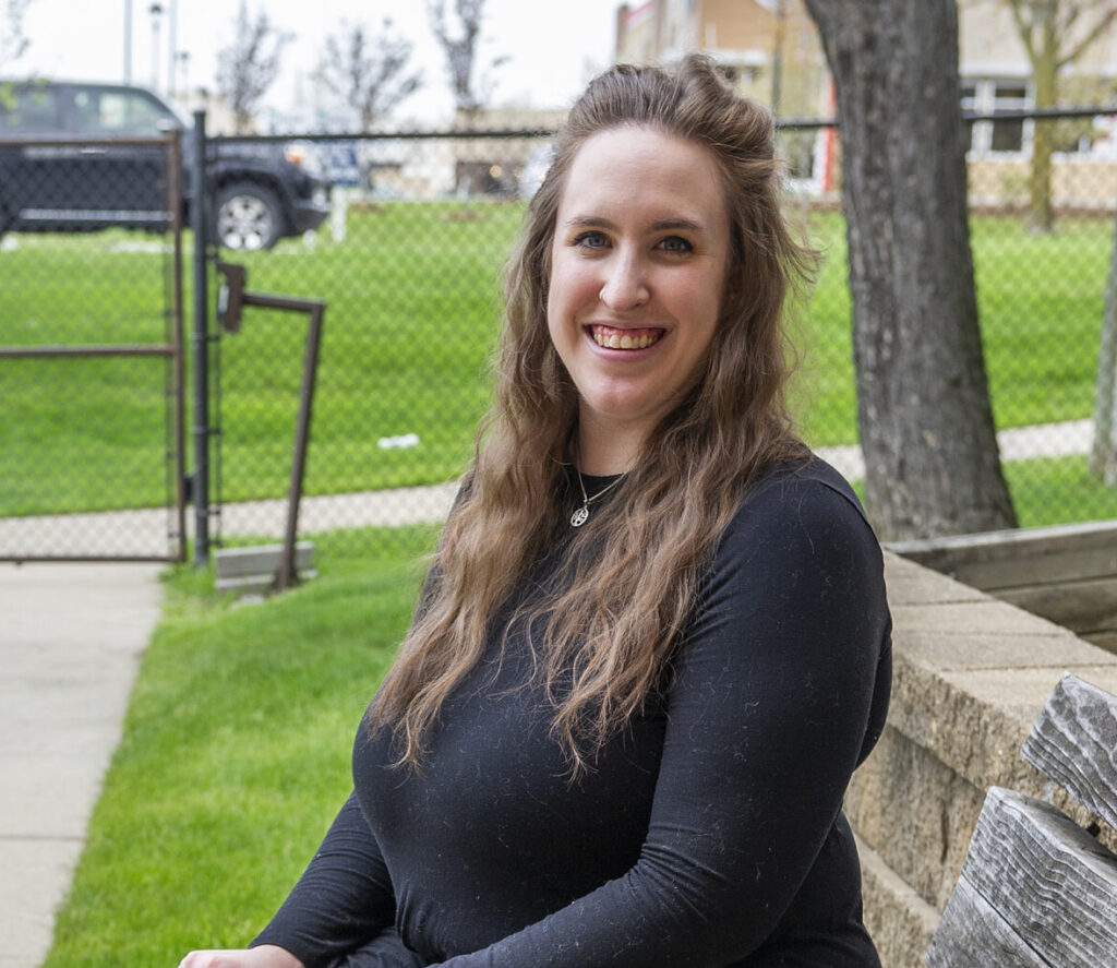 A woman in a black dress sits on a bench next to a golden retriever wearing a bandana.