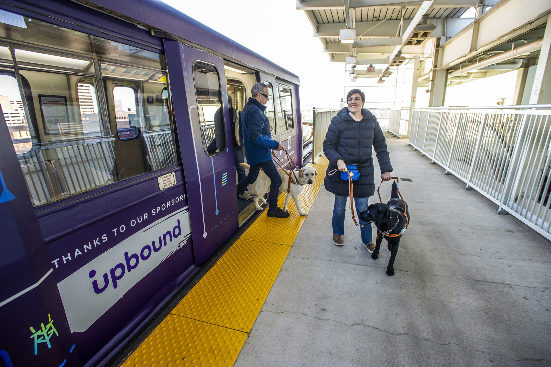Passengers exit a train while accompanied by two dogs at a station.