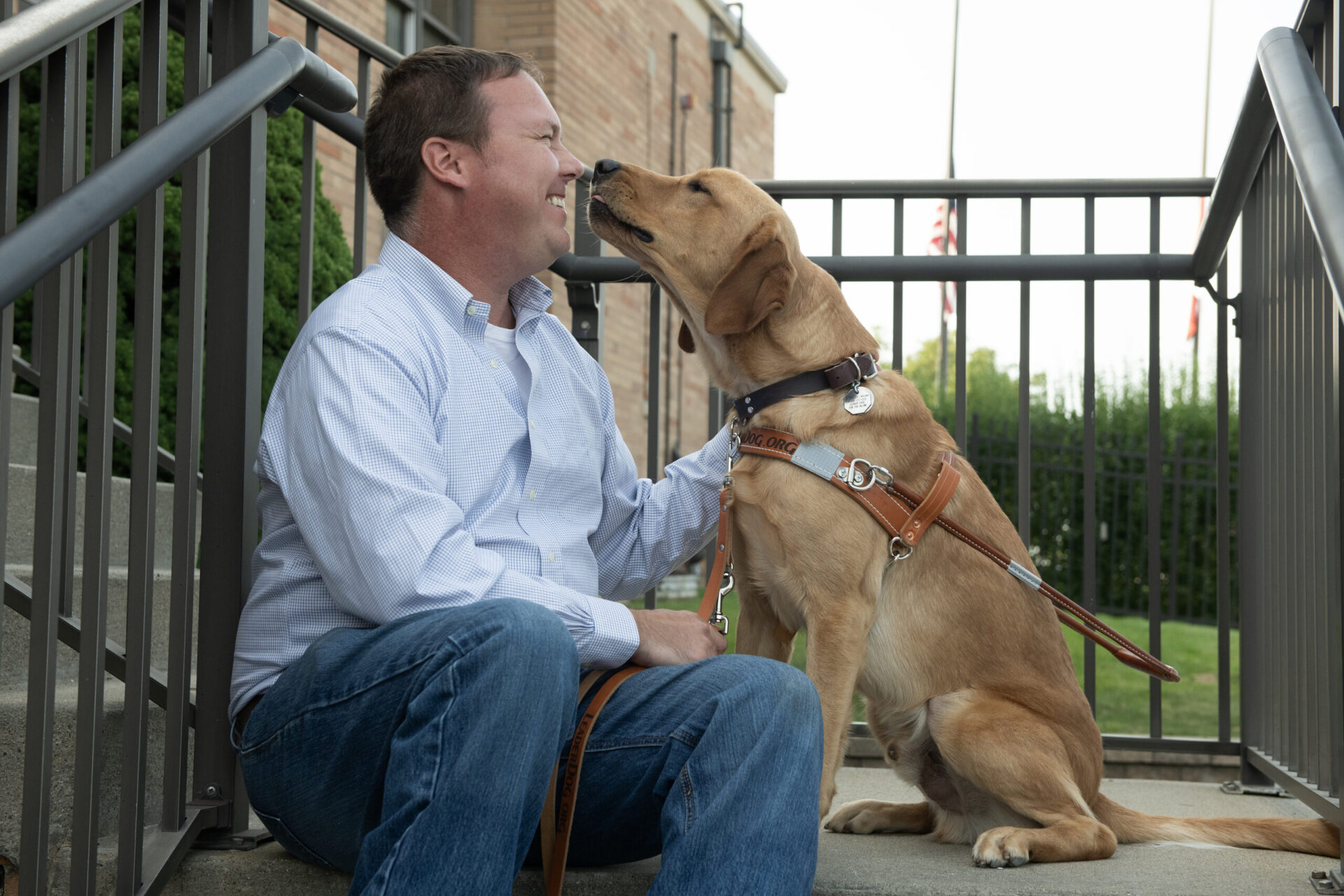 A man joyfully interacts with a golden retriever, sharing a moment of affection while seated on steps.