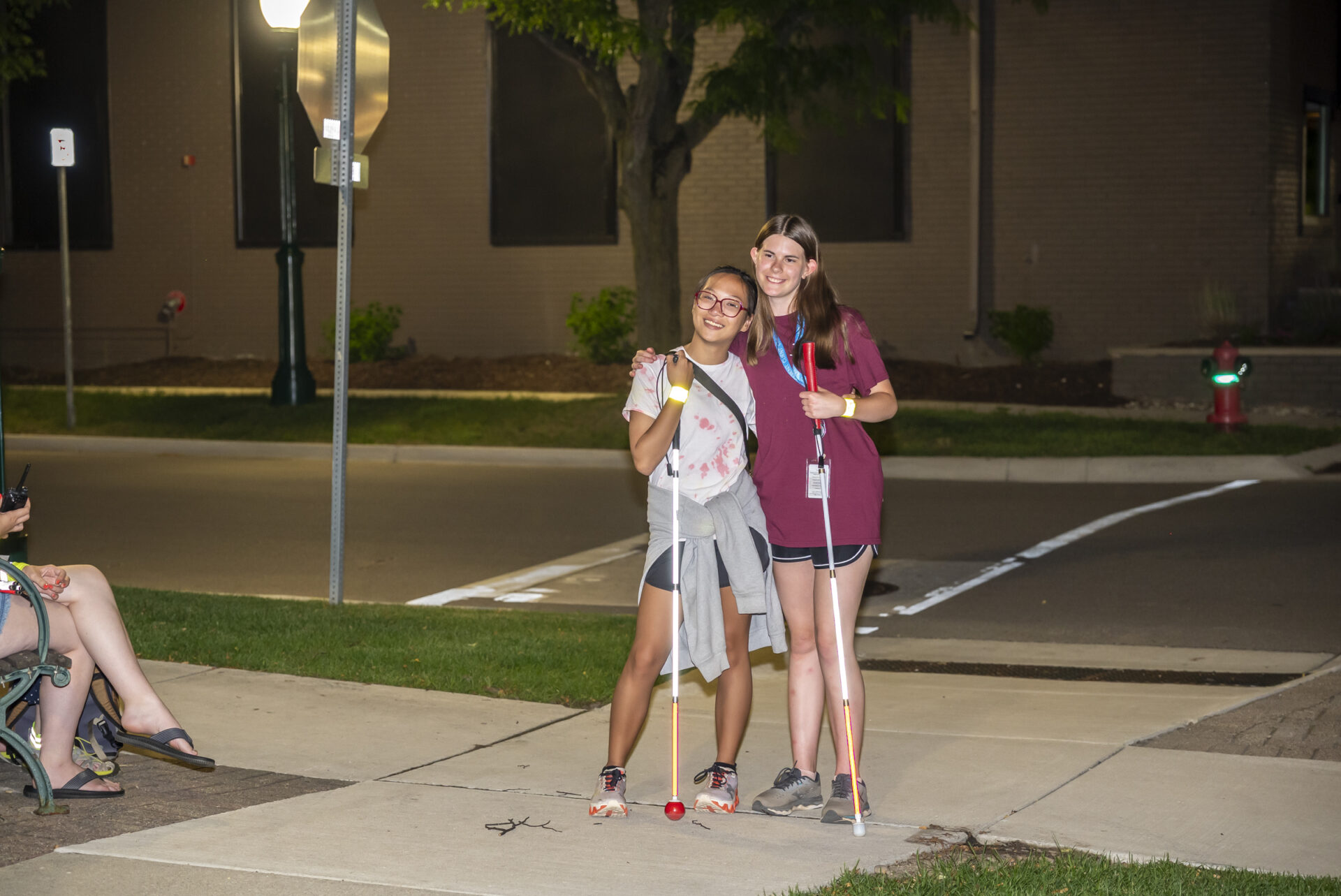 Two teen girsl each holding a white cane smile toward the camera while hugging.