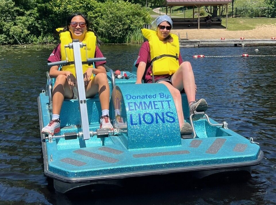Two individuals enjoy a ride on a bright blue paddle boat equipped with life jackets on a calm body of water.