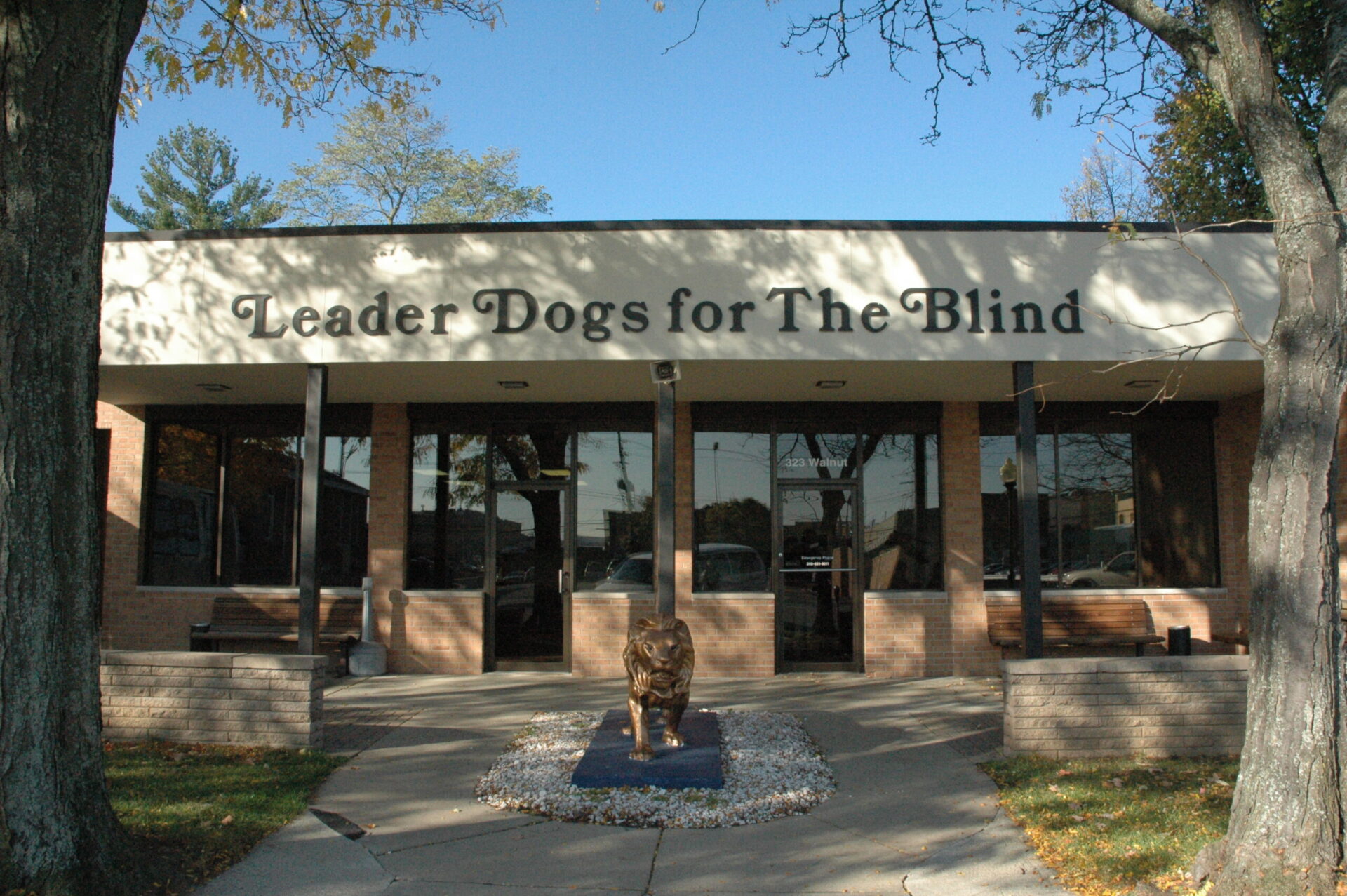 A building with the sign "Leader Dogs for The Blind" prominently displayed above its entrance, featuring a sculpture in the foreground.