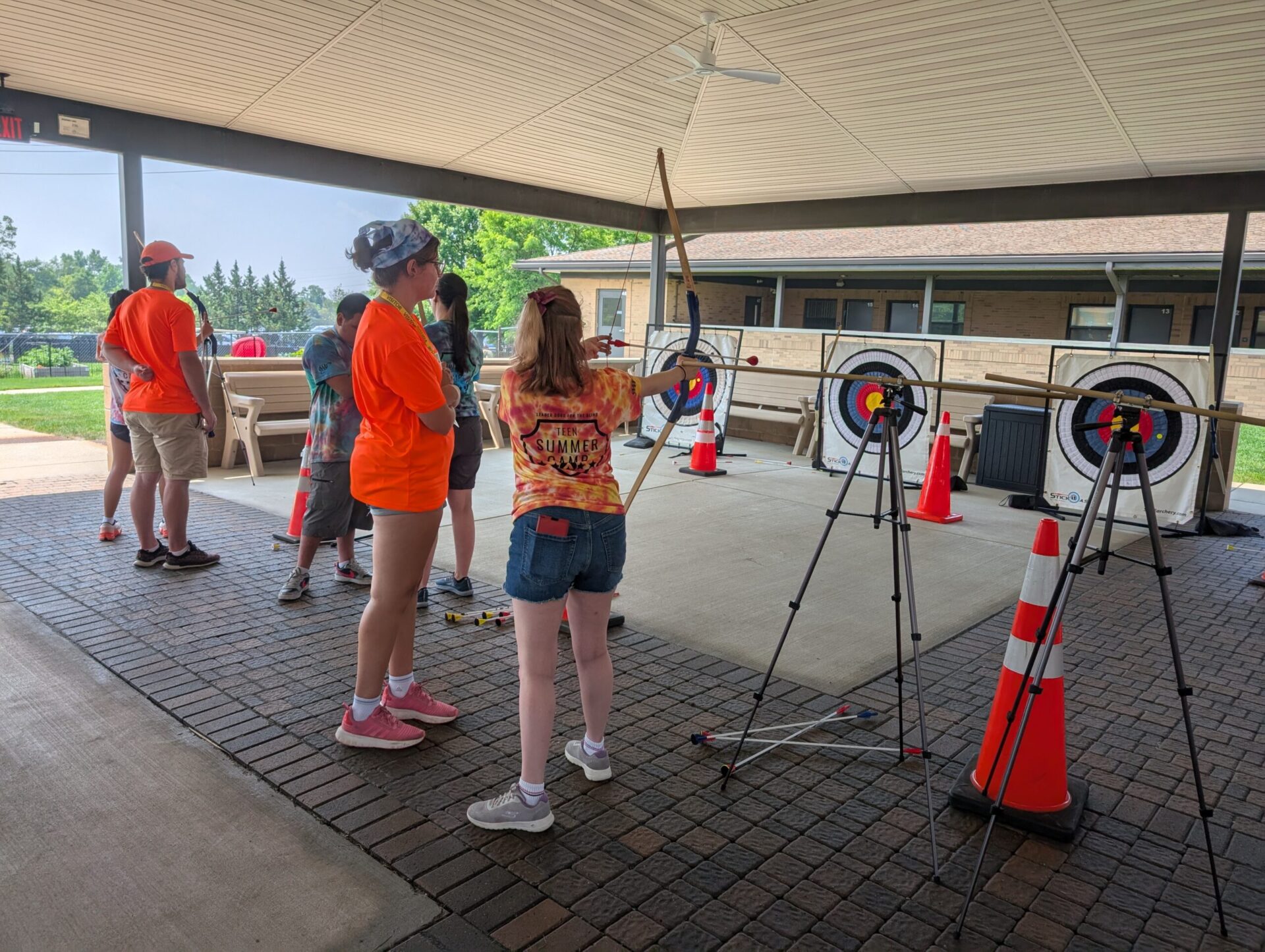 A group of teens practice archery in a covered area.
