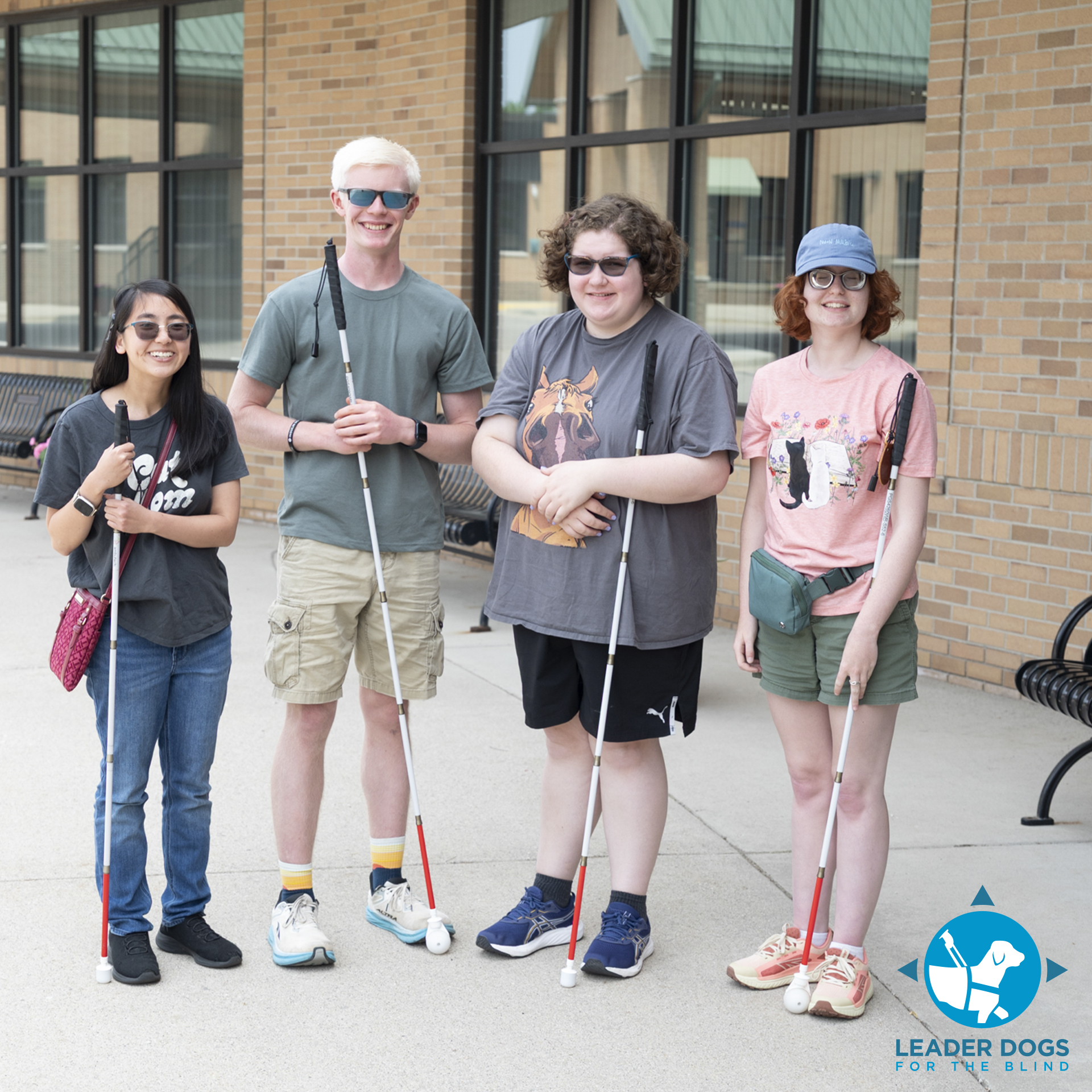 A group of individuals stands together outside, each holding a white cane and smiling.