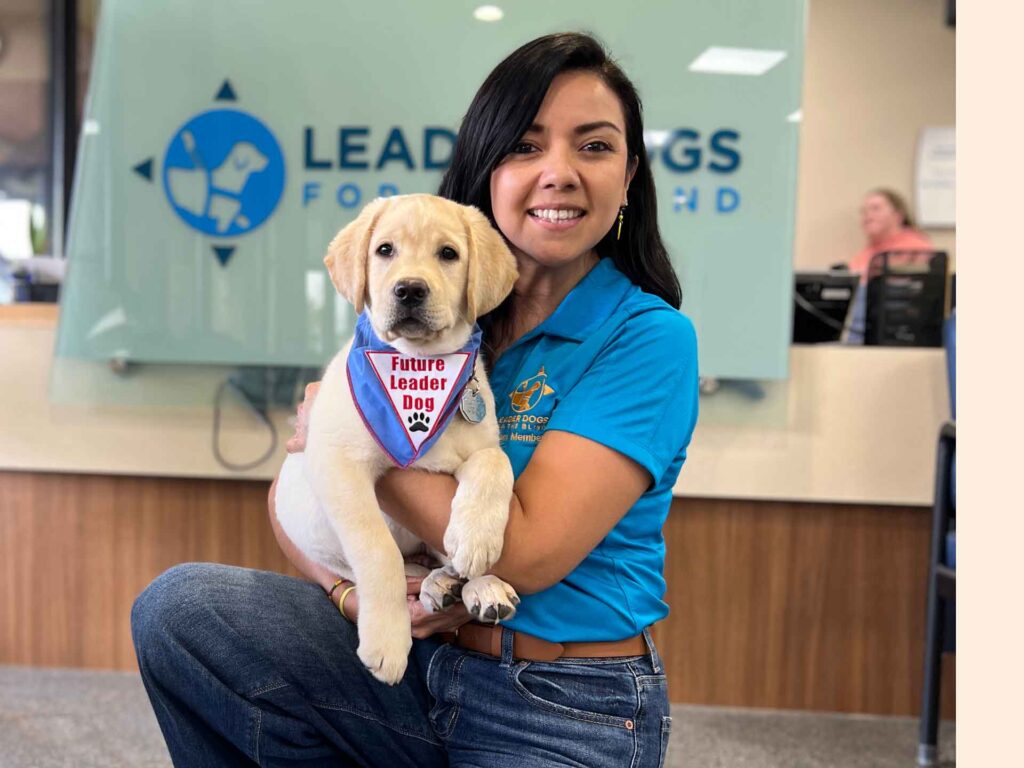 A woman smiles while holding a puppy adorned with a 