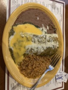 A yellow plate holds two green enchiladas, rice and refried beans