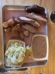 An aluminum tray lined with butcher paper holds barbecued ribs, brisket, sausage, beans, and cole slaw.