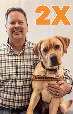 A man sits with his arm around a yellow Lab Eader Dog. The graphic "2X" is visible over the image.