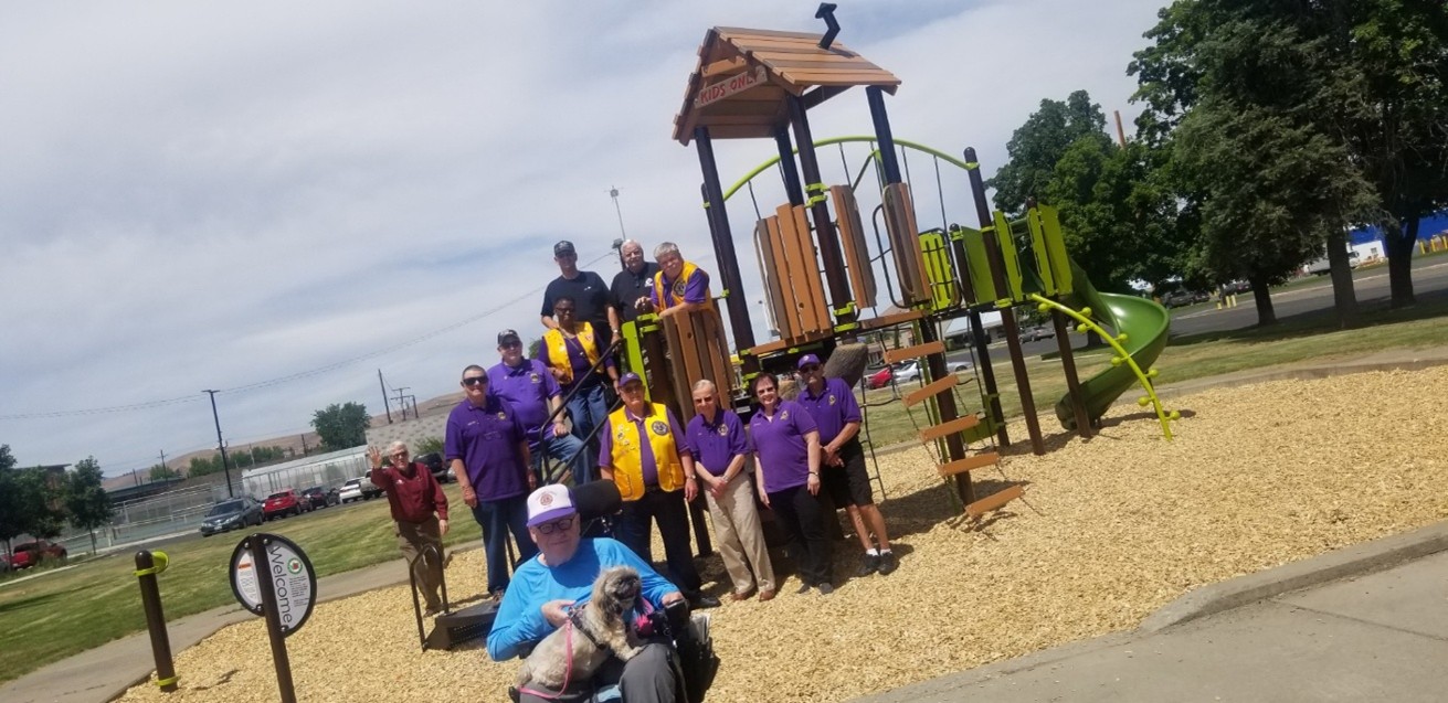 A group of adults stand by a kids playground outdoors smiling toward the camera.