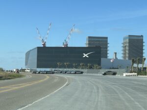 A large, black building centered with a beautiful blue sky. The Space X symbol is seen at the top right of the building.