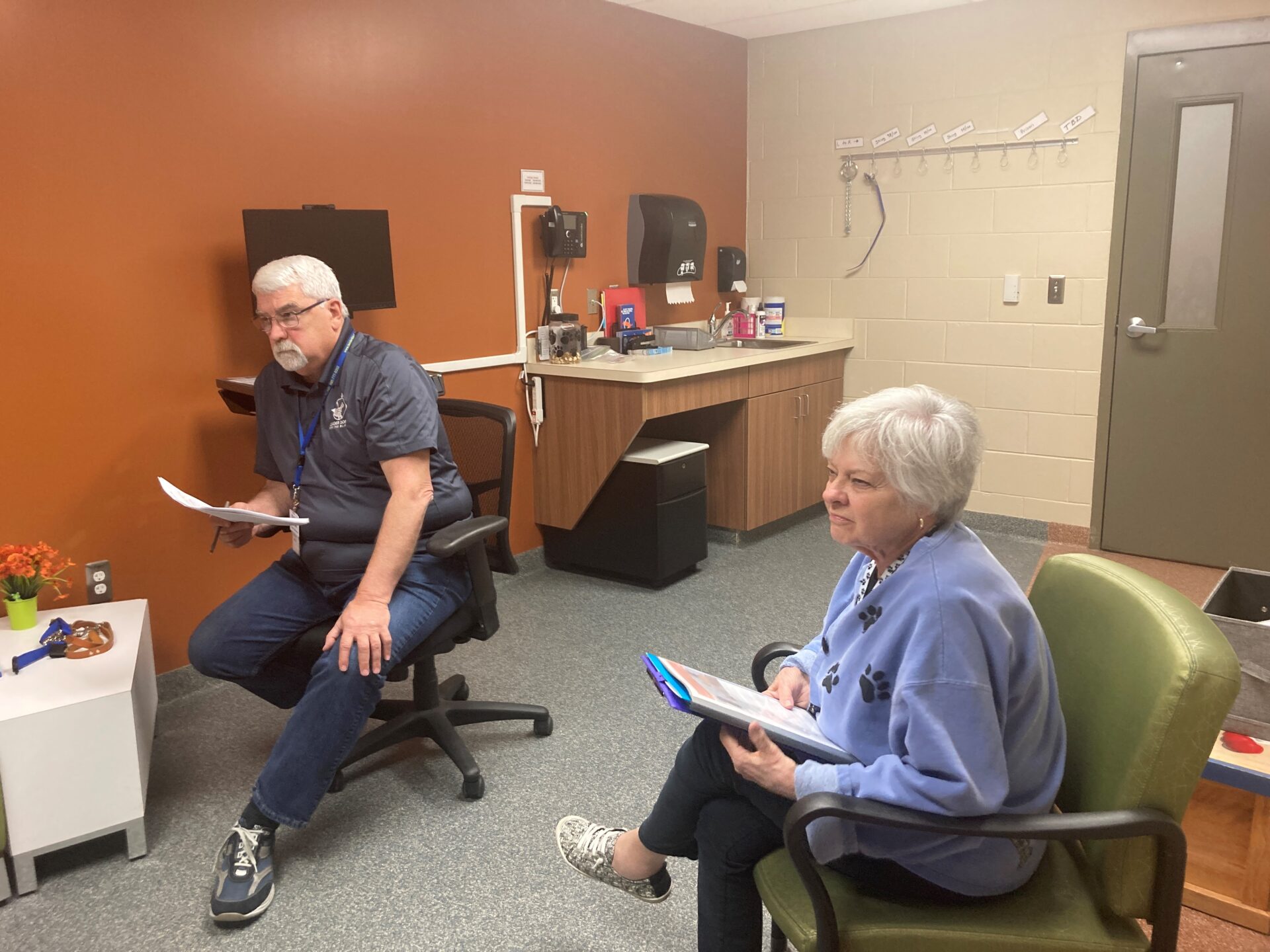 Two adults sit in chairs holding papers in an office of the Canine Development Center.