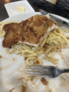 A half-eaten plate of schnitzel and spaetzle on a white plate.