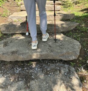 A closeup of a women's feet as she hikes uneven rock steps using a white cane in one hand and a trekking pole in the other.