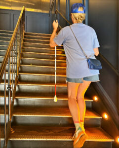 A woman ascends the right side of a lighted staircase with a white cane in her left hand.