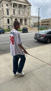A man uses his white cane to navigate the sidewalk across from a courthouse