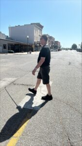 A man uses a white cane to cross a quiet downtown street.