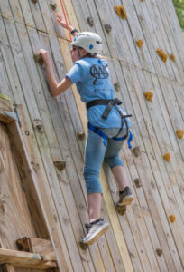 A teen in a harness and helmet solo climbs a rock wall.