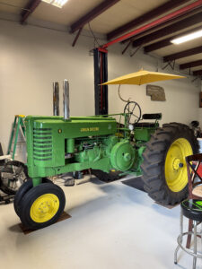 A bright green vintage John Deere tractor sits inside a shop.