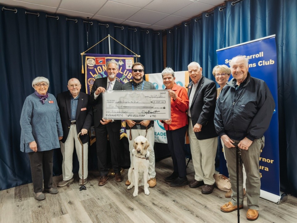 A group of people hold up a large check. In the center of the group is client Walker with his yellow lab Loki