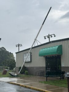 Oversized golf club sculpture displayed outside a golf and miniature golf facility on a rainy day, with the club leaning high above the building entrance and a large golf ball positioned near the base.