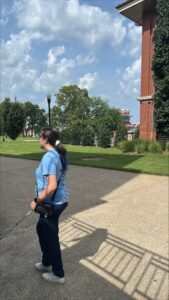 A person walks with their cane across campus. Big Red is displayed on the upper façade of the football stadium in the background.