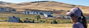 A woman in the foreground of a panoramic photo of more amber waves of grain and a deep blue sky, despoiled with houses.