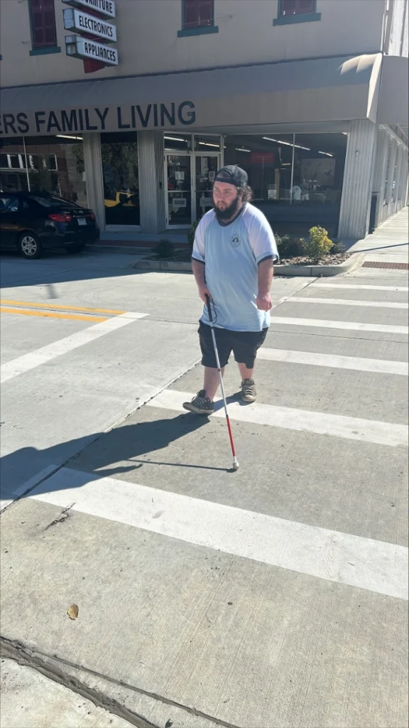 Wearing a baseball-style shirt, shorts and a backwards cap, Moredecai uses his cane to cross a street in downtown Russellville. He also has a great beard!