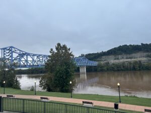 The Ohio River runs along a limestone bluff and under a traffic bridge. It is a muddy brown due to lots of rain upriver.