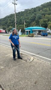 A person uses a white cane on the sidewalk along Lake Street. She is wearing a Kentucky blue t-shirt and jeans.