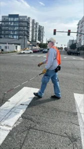 Wearing a gray sweatshirt and jeans, a person uses his white cane while crossing a street