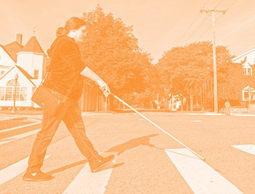 Orange colored image of a woman crossing a street with a white cane