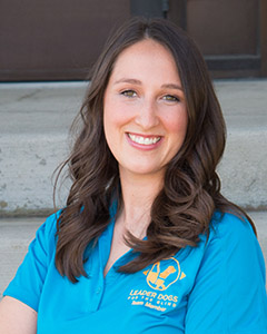 Kristy smiles at the camera. She has long, brown hair. She is wearing a bright blue polo with the Leader Dog logo in yellow.