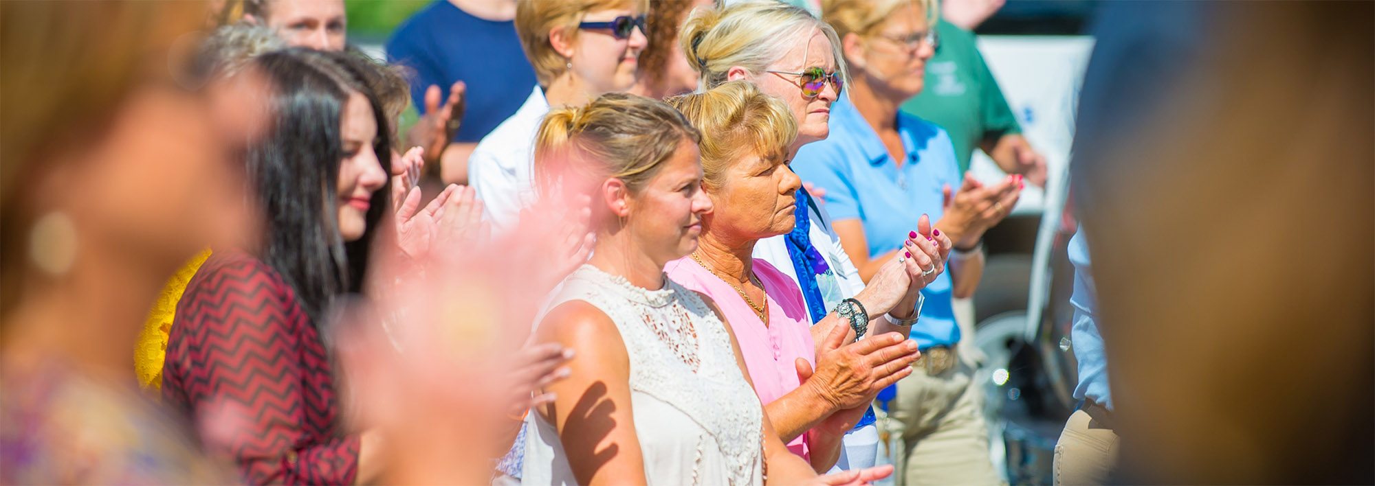 A crowd of people standing and clapping in the bright sunlight