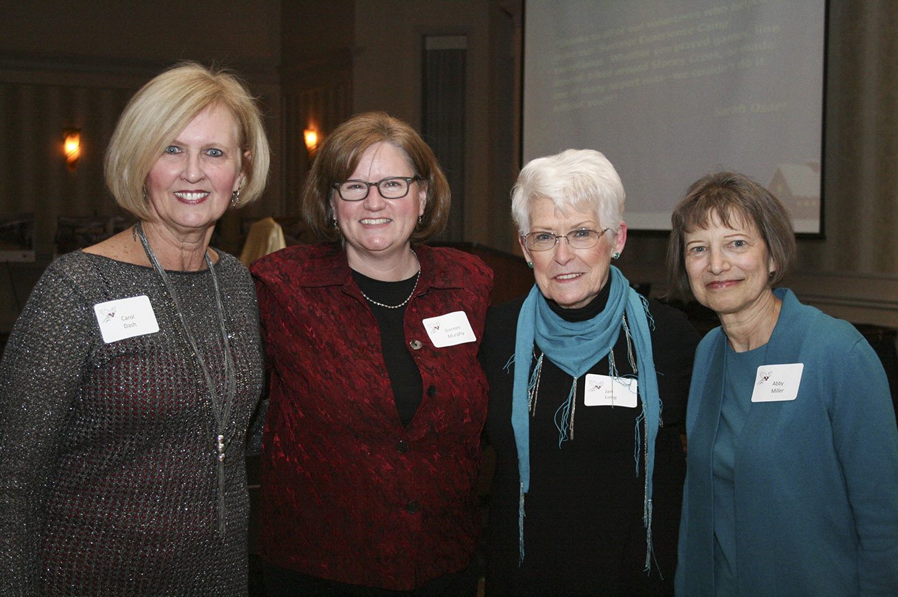 Four women stand smiling at the camera with their arms around each other